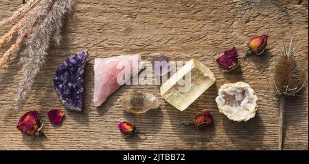 Amethyst druzy, rosa Quarz, Quarz mit Rutil, Fluorit, Calcit, Quarz in Geode Mineralsteine auf dem Holztisch mit trockenen Blumen aufgestellt. Gemsto Stockfoto