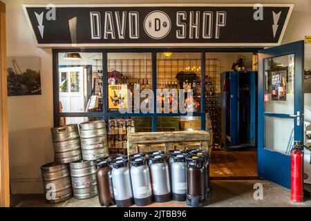 Der Davo Shop der Davo-Brauerei in Deventer, einer von neun historischen Hansestädten an der IJssel, Provinz Overijssel, Niederlande, zeigt Bierflaschen, T-Shirts und Geschenkkörbe in seinem Schaufenster; leere Bierfässer und graue Fässer stehen davor. Stockfoto
