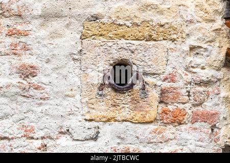 Ein rundes Loch mit einem eingebetteten Eisenring durchbricht eine Fassade im Bergkwartier, dem historischen Altstadtviertel von Deventer, einer von neun historischen Hansestädten an der IJssel, Provinz Overijssel, Niederlande. Solche Löcher finden sich in gegenüberliegenden Häusern entlang der engen Gassen von Deventer: während Belagerungen wurden Ketten über die Gassen gespannt, um feindliche Reiter daran zu hindern, durchzukommen. Stockfoto