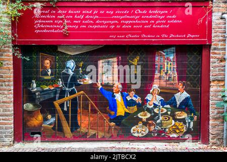 Ein Wandbild an einer roten Tür zeigt eine Szene aus Charles Dickens' "die Pickwickians". Mehrere Leute sitzen an einem Tisch, ein Diener serviert Essen. Ein Porträt von Charles Dickens ist in das Gemälde integriert. Darüber befindet sich ein rotes Schild mit niederländischem Text über alte Gasthäuser und Dickens. Das Kunstwerk ist in Deventer, Niederlande, im Bergkwartier zu sehen Stockfoto