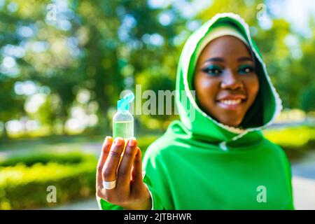 Multikulturelle Rasse muslimische Frau in grünen Hijab und Nase piersing gelten ein antiseptisches Gel im Freien im Sommerpark Stockfoto