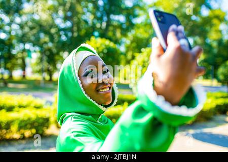 lateinamerikanische hispanic-arabische Frau in grünem muslimischen Kleid mit modernem hellen Make-up und Nasenpiercing, die Selfie an der Telefonkamera im Freien macht Stockfoto