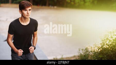 Athletischer junger Mann, der auf einigen Treppen in der Stadt läuft. Ernsthaftes Gesicht. Stockfoto
