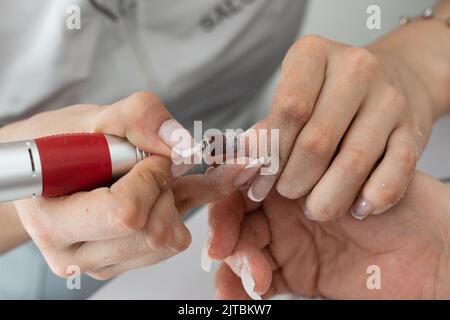 Detailaufnahme der Hände eines Manikuristen mit einem elektrischen Polierentferner, der den Polygel-Nagel formt und die Maniküre perfektioniert Stockfoto