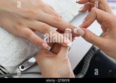 latina Manikuristin Mädchen Reinigung der Nägel eines Kunden mit einem Stück Baumwolle, nachdem sie mit einem elektrischen Nagelpuffer die Unvollkommenheiten geschliffen. Stockfoto