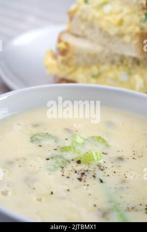 Köstliche Sellerie-Suppe mit Ei-Salat-Sandwich im Hintergrund vertikal Stockfoto