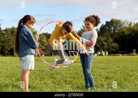 Glückliche Kinder springen durch den Hula Hoop Reifen im Park Stockfoto