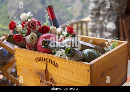 Holzkiste mit leeren Weinflaschen, Früchten und Blumen, Nahaufnahme, geringe Tiefe, Flaschen im Fokus, Blumen verschwommen Stockfoto