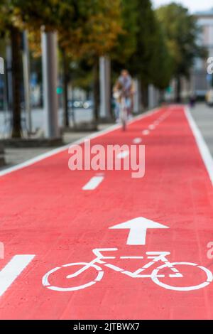 Frau, die in der Stadt entlang der roten Fahrradstraße radelt Stockfoto