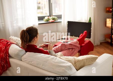 Frau schaut fern und trinkt Kaffee an weihnachten Stockfoto