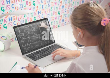 Ein Mädchen mit blondem, europäischem Auftritt in Kopfhörern lernt online von zu Hause aus und macht ihre Hausaufgaben. Ein Teenager mit Fernunterricht Stockfoto