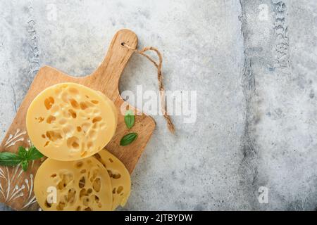 Käse Maasdam oder Radamer. Stück Käse auf Holzstanda auf altem grauen Betonhintergrund. Draufsicht. Freier Speicherplatz für Ihren Text. Stockfoto