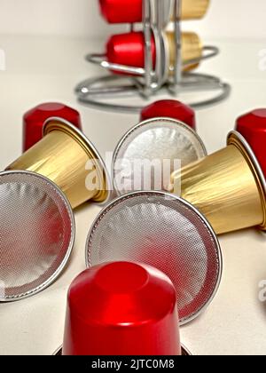 Eine vertikale Nahaufnahme von roten und goldenen Kaffeekapseln auf einer weißen Oberfläche Stockfoto
