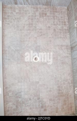 Ein Duschboden mit neutralen, hellbeigen quadratischen Fliesen und silbernem Metallabfluss Stockfoto