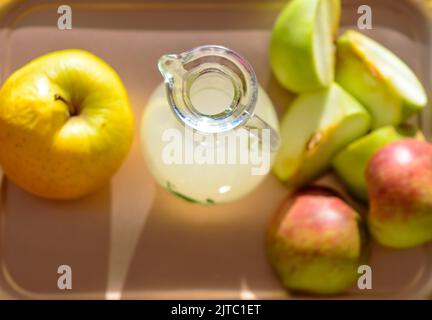 Apfelessig in einer Glasflasche und Scheiben von frischen gelben Äpfeln und grünen Äpfeln auf hellem Hintergrund. Draufsicht. Stockfoto