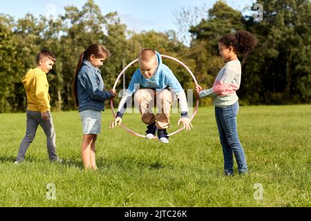 Glückliche Kinder springen durch den Hula Hoop Reifen im Park Stockfoto