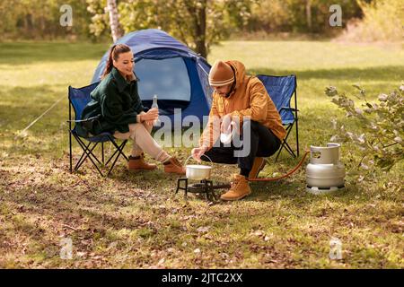 Pärchen trinkt Bier und kocht Essen im Zeltlager Stockfoto