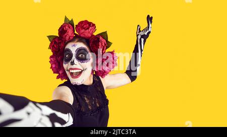 Frau mit gemaltem Schädel auf dem Gesicht nimmt Selfie während der Feier des Tages der Toten oder Halloween. Stockfoto