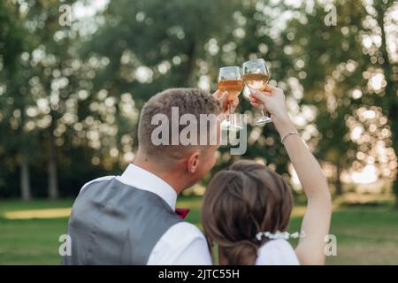 Freuen Sie sich auf ein glückliches verheiratetes Brautpaar im Hochzeitskleid und einen Bräutigam im Anzug, der zusammen Sekt trinkt Stockfoto