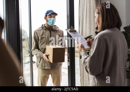 Delivery Mann in Maske mit Box und Kunde zu Hause Stockfoto