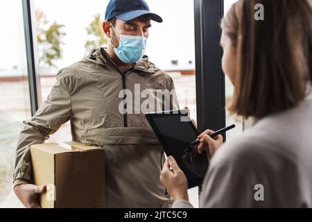 Deliveryman in Maske und Frau Unterzeichnung digitale Form Stockfoto