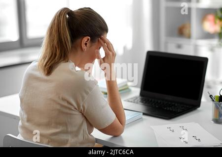 Müder Lehrer mit Laptop, der zu Hause Kopfschmerzen hat Stockfoto