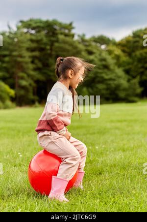 Glückliches kleines Mädchen hüpft auf Hopper Ball im Park Stockfoto