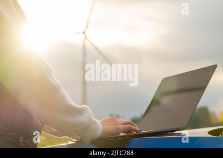 Eine Ingenieurin überprüft die Stabilitätsarbeit der Windmühle mit einem Laptop auf dem Feld bei Sonnenlicht. Grüne Energie der Zukunft Stockfoto