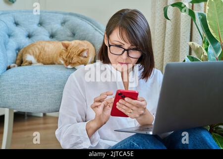 Frau, die zu Hause mit einem Laptop sitzt, Ingwer-Katze, die auf einem Sessel schläft Stockfoto