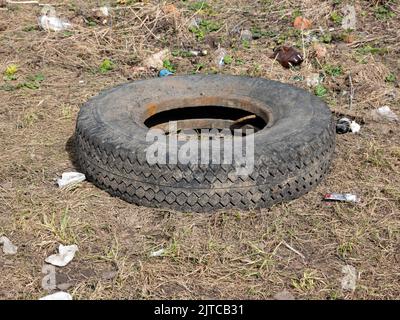 Ein abgenutzter Autoreifen schwelt im Schlamm und eine Pfütze auf dem Boden. Umweltverschmutzung. Ökologische Probleme. Stockfoto