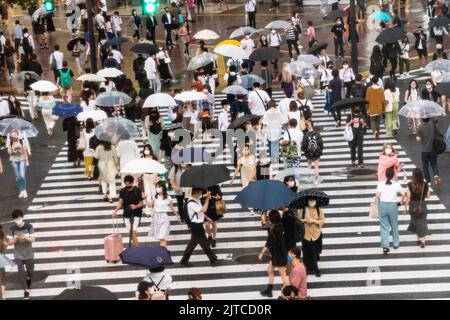Fußgänger mit Regenschirmen überqueren die multidirektionale Kreuzung, die als Shibuya Crossing in Shibuya ward, Tokio, Japan, bekannt ist. Die Kreuzung gilt als die verkehrsreichste Fußgängerkreuzung der Welt. Stockfoto