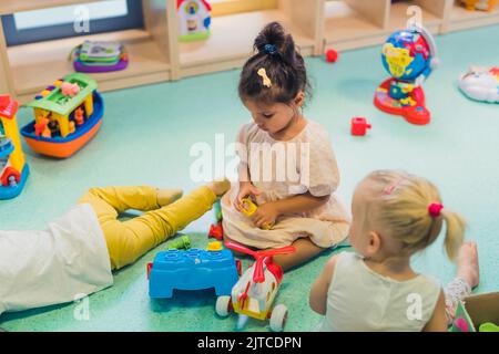 Kleinkinder, die mit einem Spielzeug für Sortierer in Kunststoffform, einem farbenfrohen Hubschrauber, Booten und anderen Spielzeugen spielen. Arbeit an Problemlösungsfähigkeiten, Entwicklung von Feinmotorik und grobmotorischen Fähigkeiten durch sensorisches Spielen im Kindergarten. Hochwertige Fotos Stockfoto