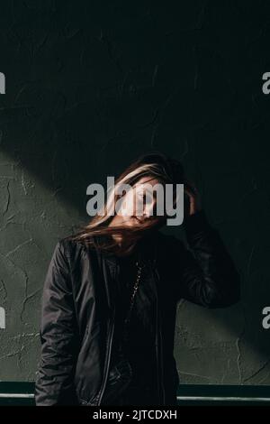 Ein junges Mädchen in einer schwarzen Jacke steht an der Wand eines Gebäudes Stockfoto