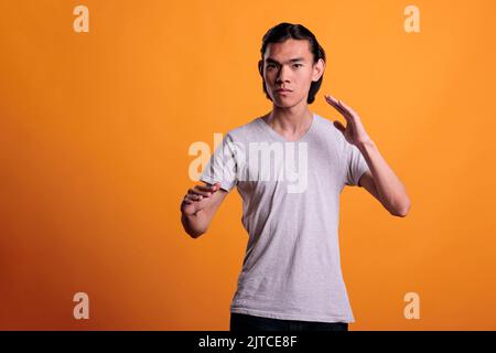 Ernst starke junge Erwachsene asiatische Mann in Karate kämpfen Pose Porträt stehen. Teenager in Angriffsposition, der Kampfkunst übt, ruhiger, selbstbewusster Kämpfer, der die Kamera anschaut Stockfoto