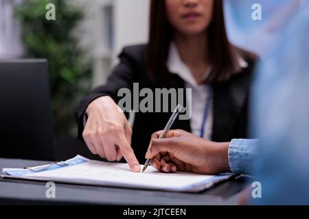 Person, die die Berichtsdateien an der Rezeption ausfüllt, Registrierungsformulare vor der Teilnahme an einem Termin für den Kontrollbesuch unterschreibt. Frau, die mit der Rezeptionistin Checkup-Papiere schrieb, Unterstützung im Gesundheitswesen. Nahaufnahme. Stockfoto