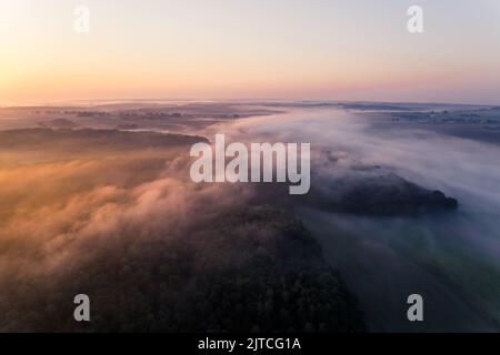 Dichter Nebel breitet sich während des farbenfrohen Sonnenaufgangs über Wald- und Bauernfeldern aus. Orangefarbene Blendung. Landspitze von Roztocze Polen. Horizontale Aufnahme. Hochwertige Fotos Stockfoto