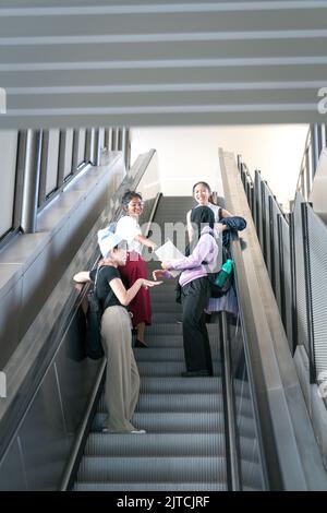 Eine Gruppe glücklicher junger Studentinnen, die die Rolltreppe hochgehen. Zurück zum College-Konzept. Stockfoto
