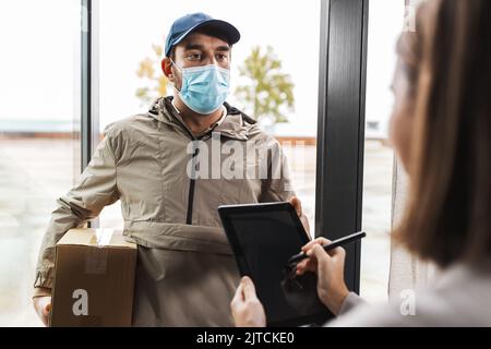 Deliveryman in Maske und Frau Unterzeichnung digitale Form Stockfoto