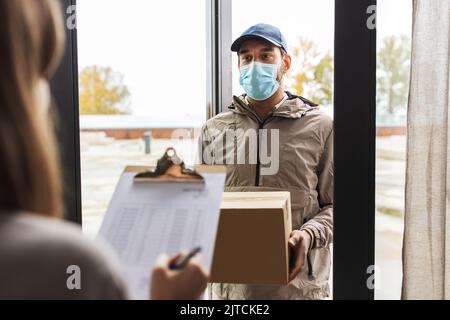 Delivery Mann in Maske mit Box und Kunde zu Hause Stockfoto