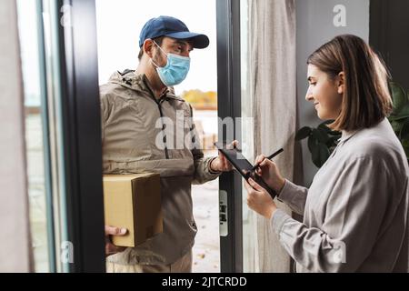 Deliveryman in Maske und Frau Unterzeichnung digitale Form Stockfoto