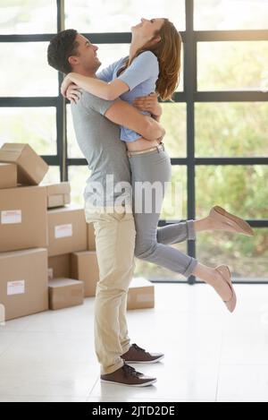 Wir haben es endlich geschafft. Ein glückliches junges Paar genießt einen unbeschwerten Moment, während es gemeinsam in ihr neues Zuhause zieht. Stockfoto