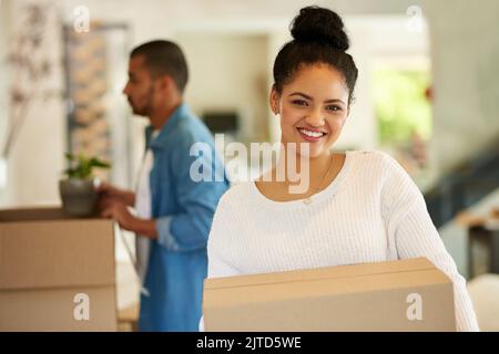 Dieser Schritt ist ein weiterer Meilenstein auf unserer Reise. Eine glückliche junge Frau trägt Pappkartons mit ihrem Freund in ihr neues Zuhause. Stockfoto
