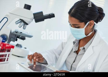 Arbeiten durch ihre neuesten Erkenntnisse. Eine junge Wissenschaftlerin, die ihre Ergebnisse auf einem digitalen Tablet aufzeichnet. Stockfoto