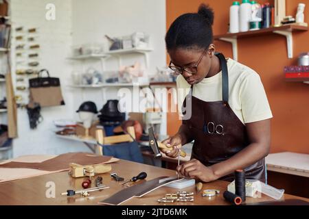 Porträt von Schwarz von weiblichen Handwerker Stanzlöcher in handgefertigten Ledergürtel in der Werkstatt, Kopierraum Stockfoto