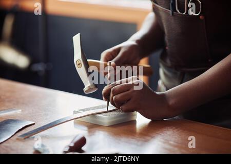 Warm getönte Nahaufnahme von weiblichen handwerklichen Stanzlöchern in handgefertigtem Ledergürtel in der Werkstatt, Kopierraum Stockfoto