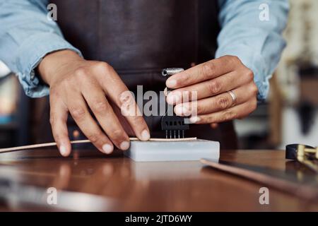 Nahaufnahme von anonymen modernen handwerklichen Stanzlöchern in handgefertigtem Ledergürtel in der Werkstatt, Kopierraum Stockfoto