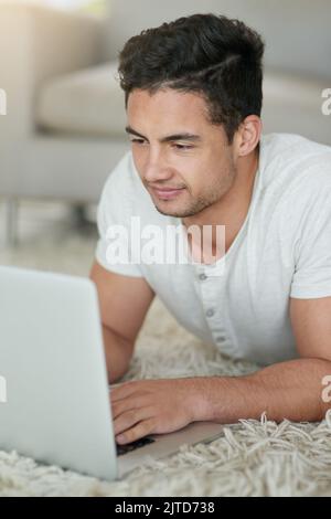 Nach der Woche ein entspannter junger Mann, der zu Hause einen Laptop auf dem Boden benutzt. Stockfoto