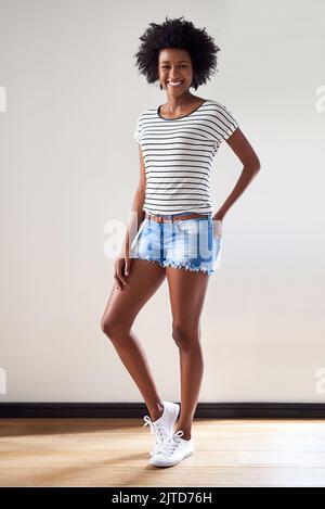 Das ist mein Wochenend-Look. Porträt einer attraktiven und glücklichen jungen Frau, die einen gestreiften Pullover und Denim-Shorts im Innenbereich trägt. Stockfoto