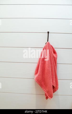 Eine weiße Shiplap-Wand mit einem korallenen Handtuch, das an einem schwarzen Haken im Industriestil hängt Stockfoto