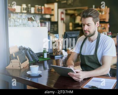 Vereinfachung des Geschäfts durch Technologie. Ein junger Barista, der in seinem Coffee Shop ein Tablet benutzt. Stockfoto